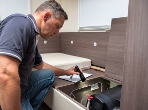 Ein Mann kniet vor einer offenen Klappe in einem Holzbettkasten, hält eine Taschenlampe in der Hand und inspiziert die Technik darunter.