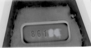 Schwarz-weiß Röntgenbild eines Metallteils mit einer rechteckigen Vertiefung in der Mitte, in der teilweise die Fahrzeug-Identifizierungsnummer „861“ zu sehen ist; rechts daneben wurden Ziffern offenbar entfernt oder überarbeitet, schweißnahtartige Spuren sind sichtbar.